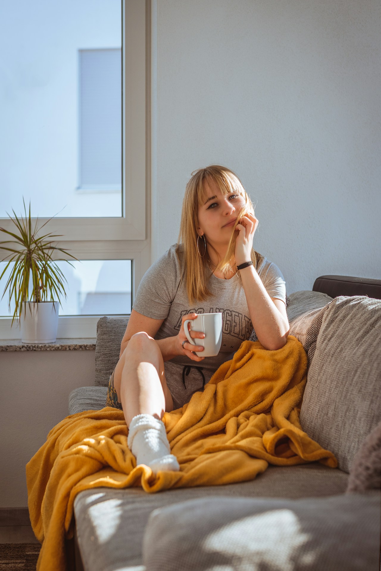 Woman resting on a couch wrapped in a blanket with coffee representing cannabis for endometriosis pain relief in Australia